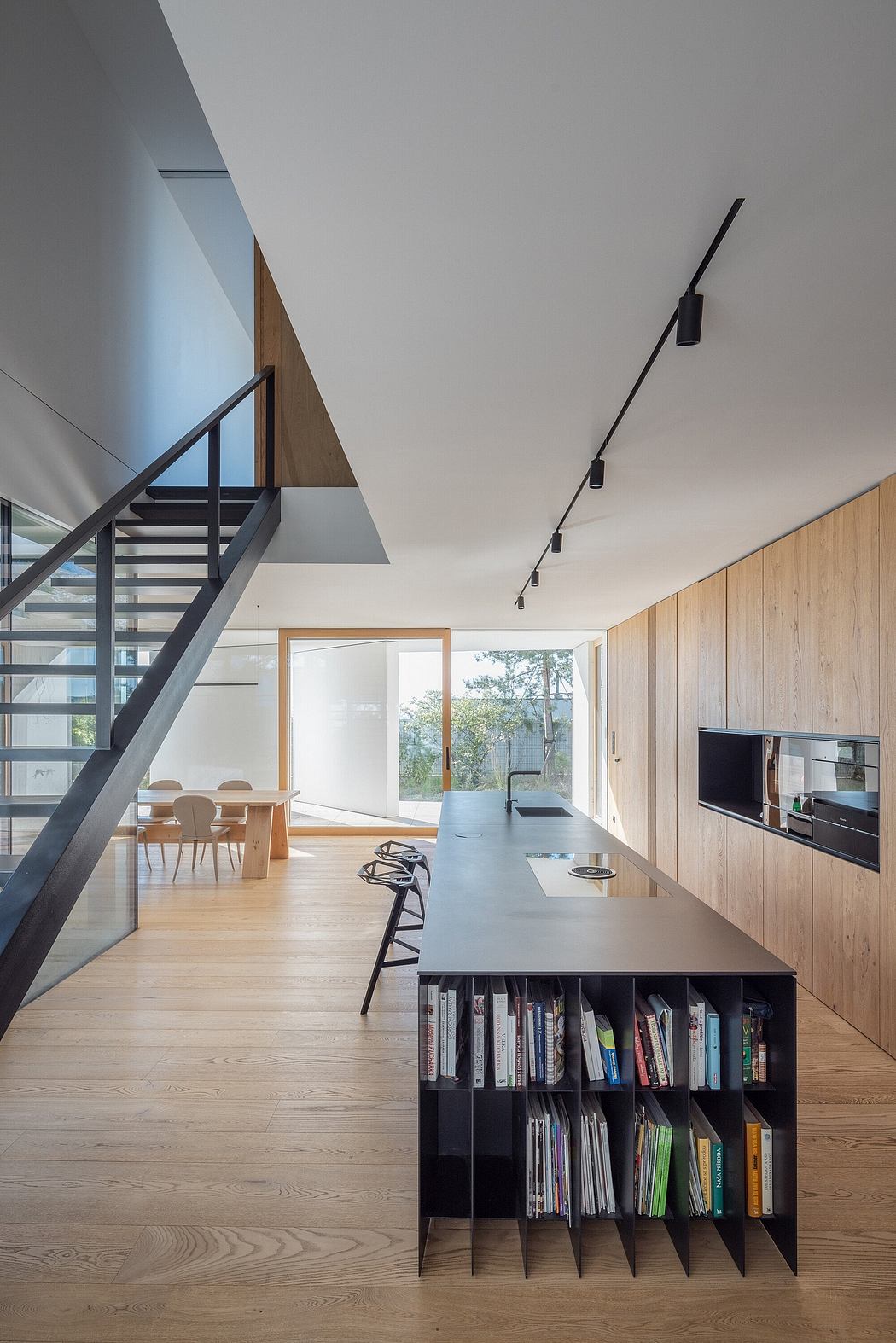 Modern, open-plan living space with wooden walls, minimalist furniture, and a sleek black staircase.