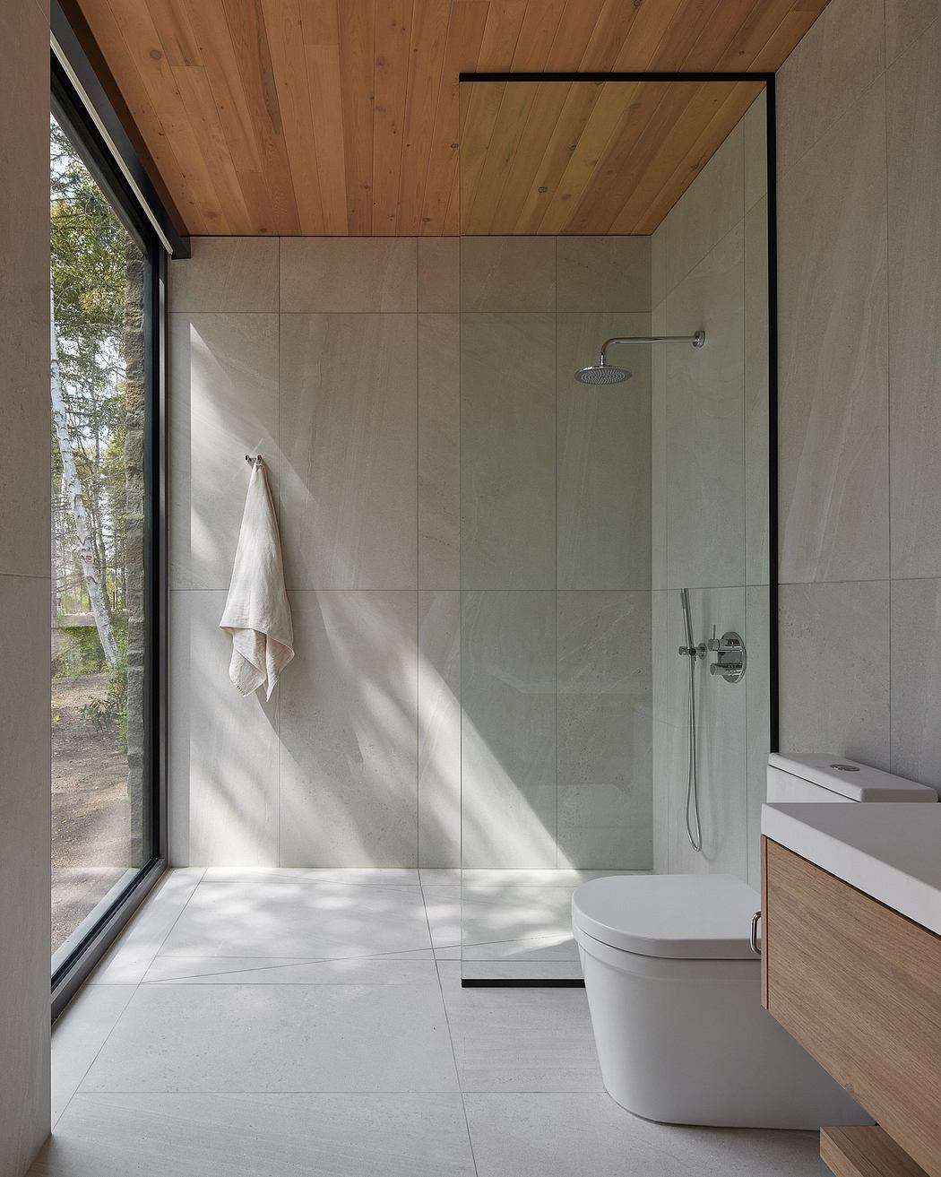 Modern bathroom with wood-paneled ceiling, glass shower, and sleek white fixtures.