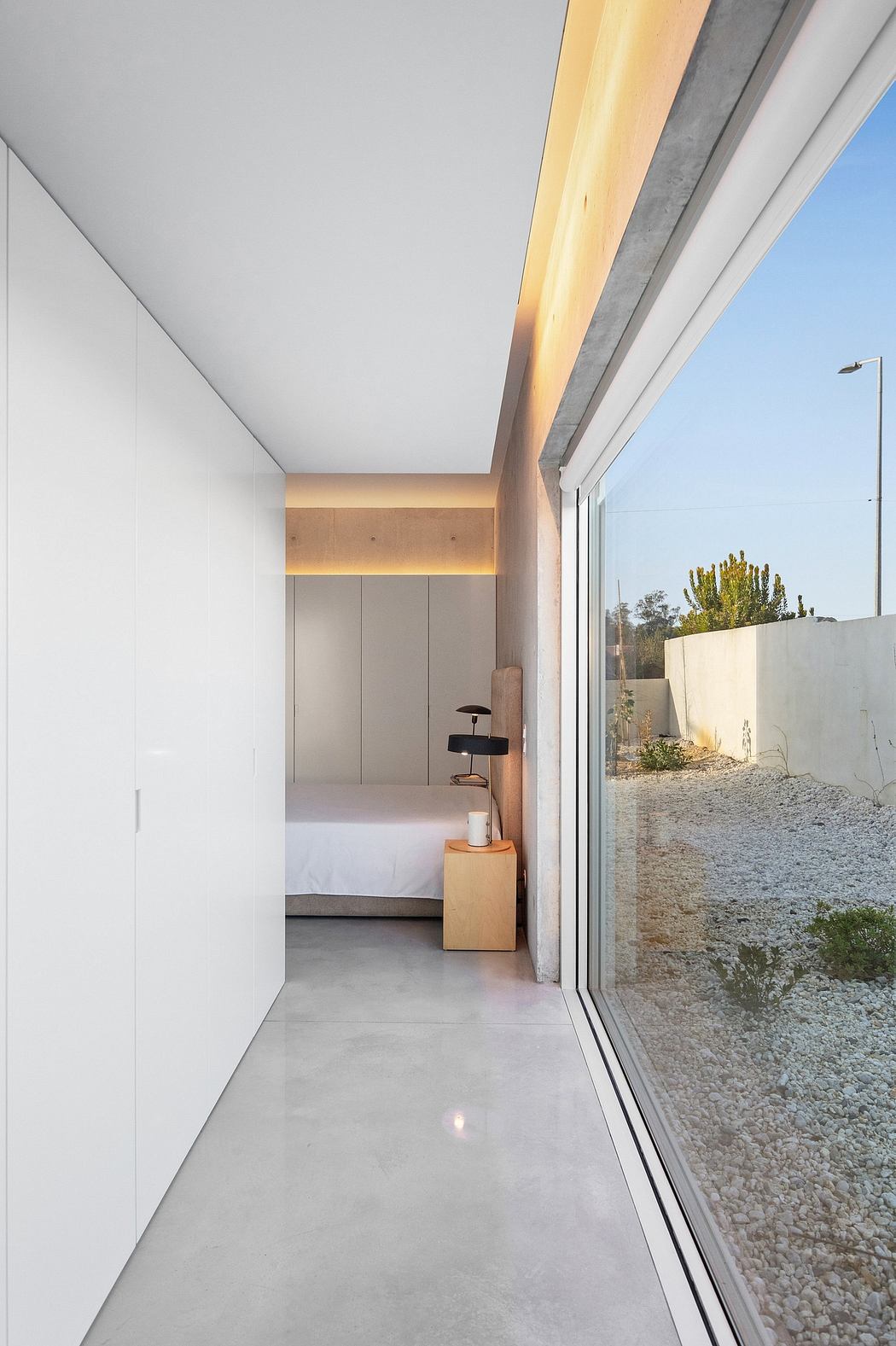 Minimalist interior design with concrete walls, floor-to-ceiling windows, and a wooden bedside table.