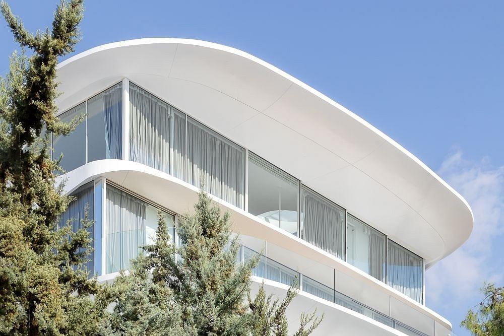 Sleek, curved facade with glass walls and balconies against blue sky and trees.