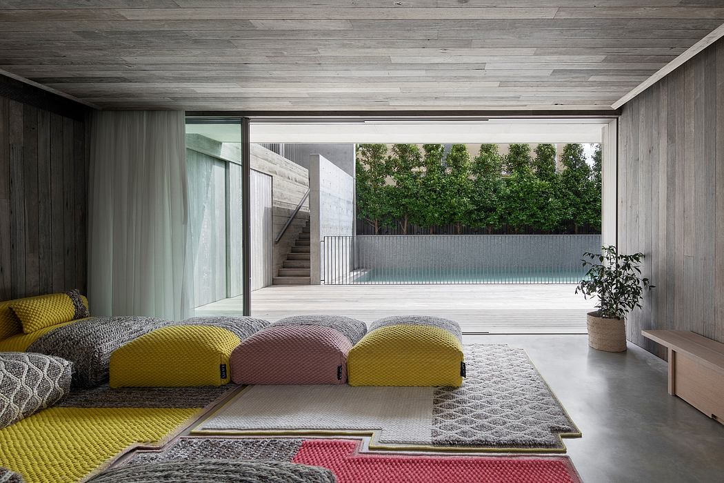 Minimalist modern interior with colorful floor cushions, concrete walls, and large glass doors overlooking greenery.