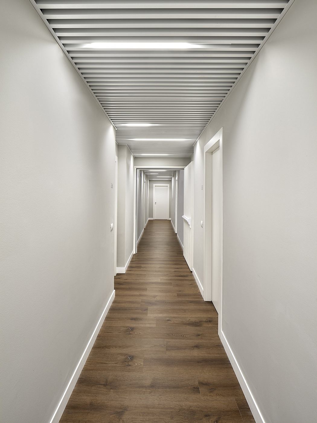 A long, minimalist hallway with wooden floors and a ceiling of parallel beams.