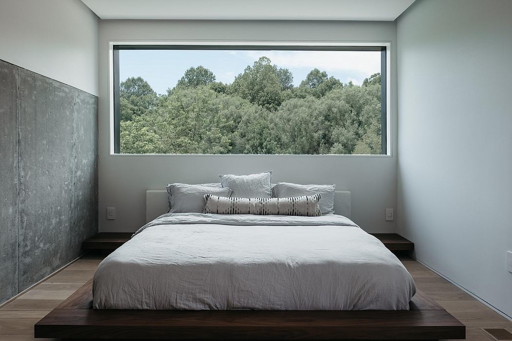 Minimalist bedroom with large window offering serene forest views, modern design.