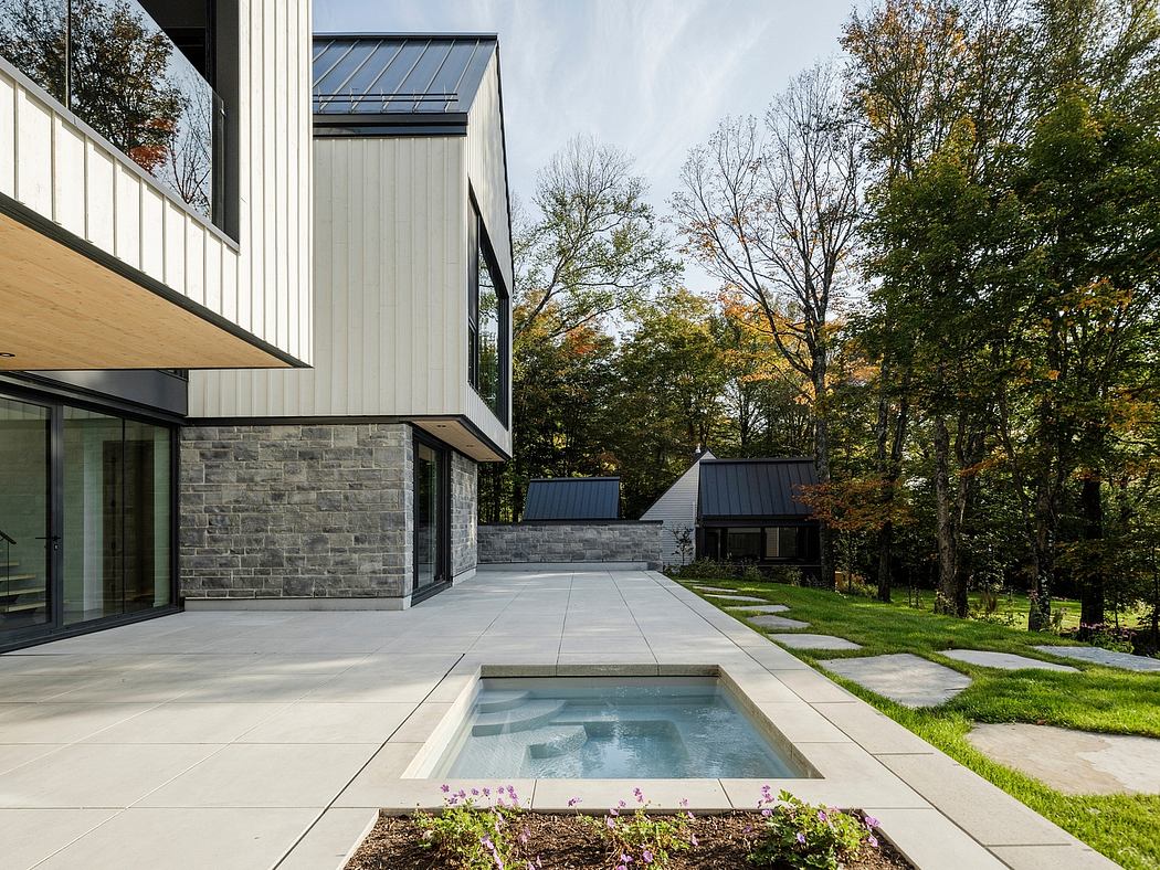 Modern, minimalist home with stone and glass exterior, private pool, and lush green surroundings.