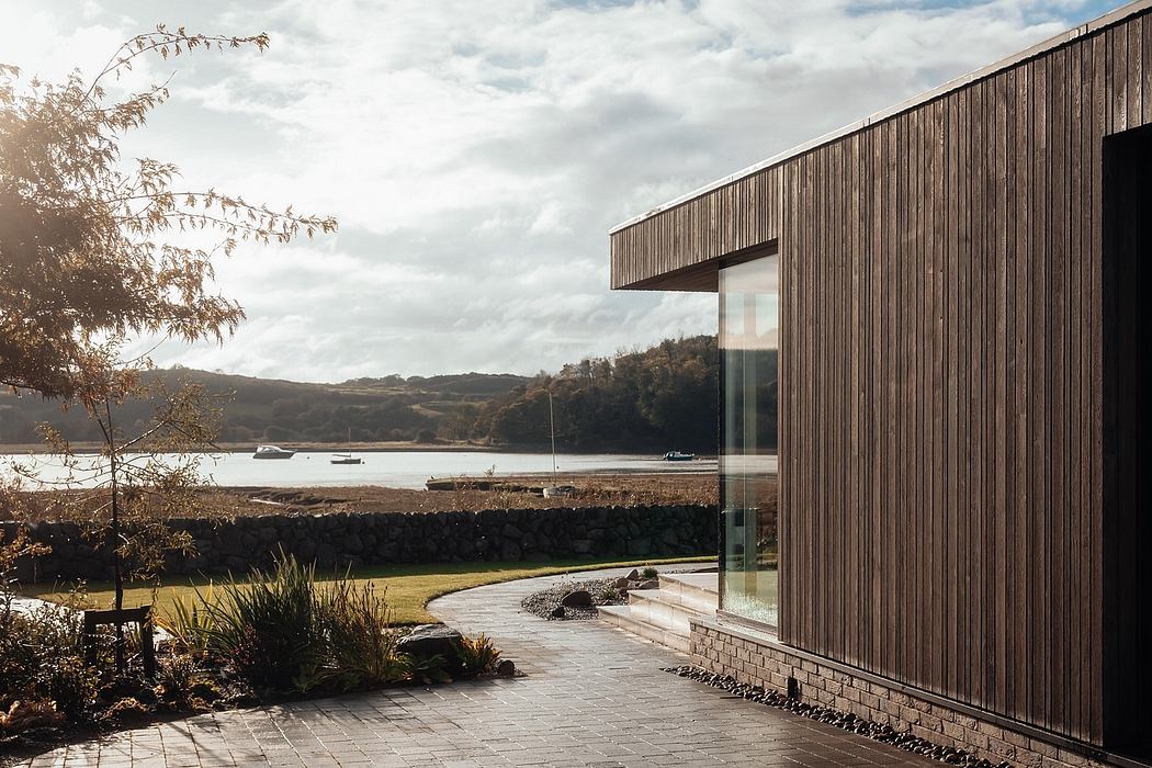 Modern lakeside home with wooden facade, glass walls, and landscaped surroundings.