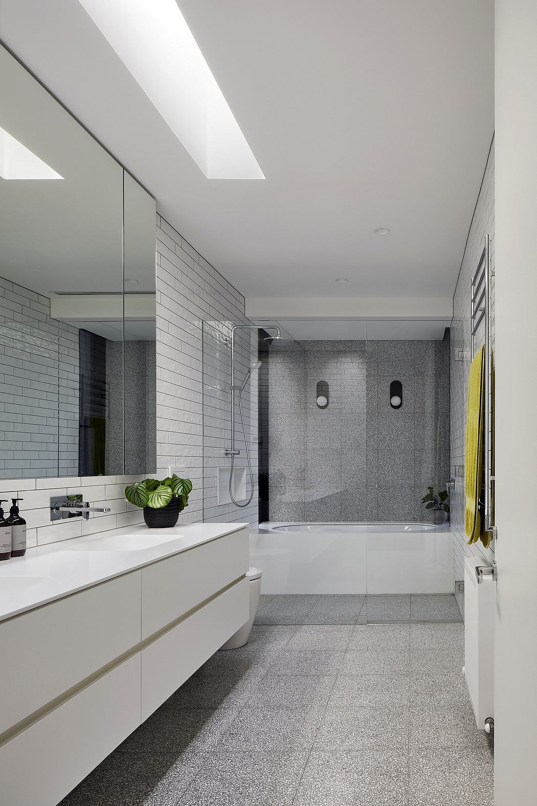 Modern, minimalist bathroom with sleek white vanity, gray tile walls, and large glass shower.