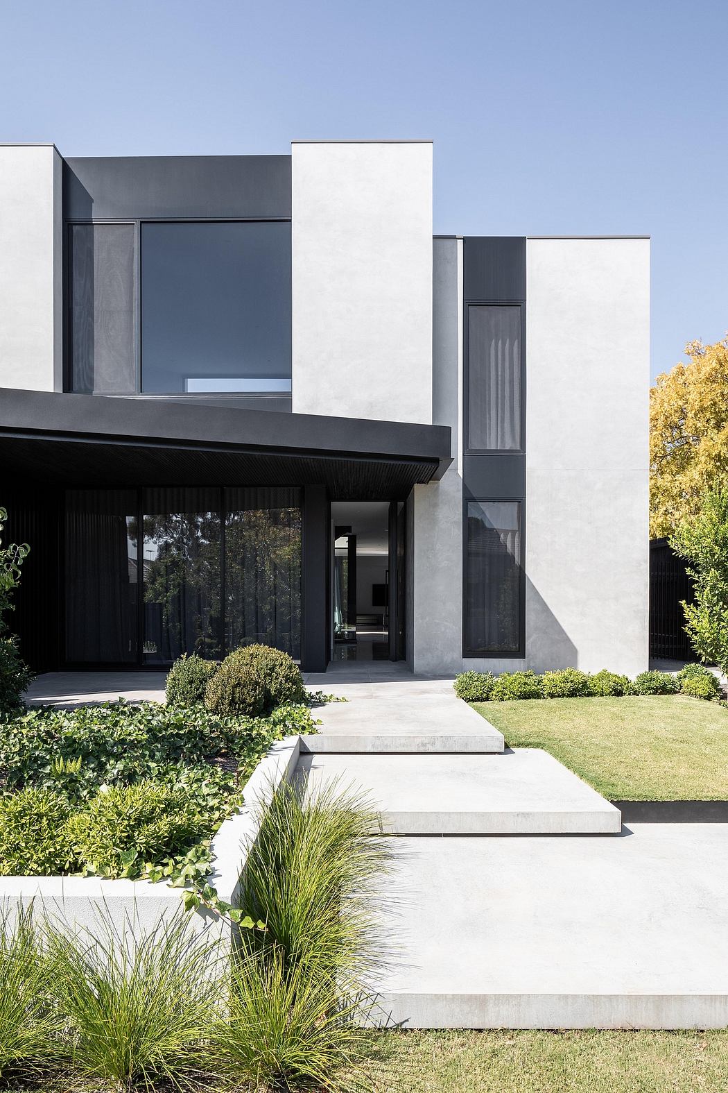The image depicts a modern, minimalist architectural design with clean lines, contrasting materials, and a well-landscaped garden.
