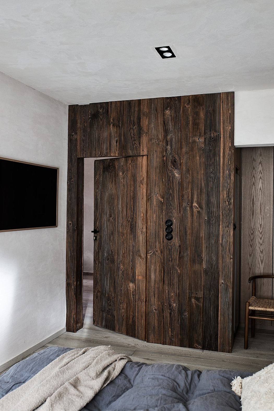 A modern bedroom with a rustic wooden accent wall and a minimalist TV setup.