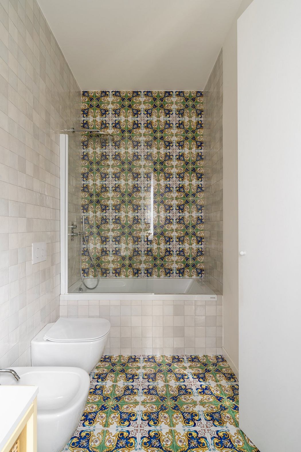 A bathroom with intricate, patterned tiles covering the walls and floor, complemented by a white toilet and bathtub.