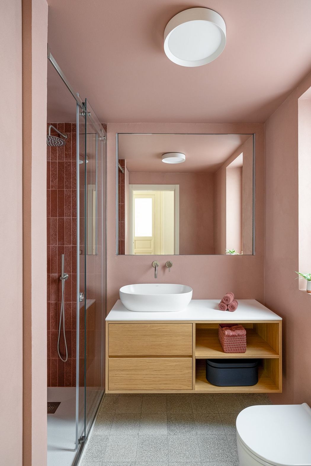 Minimalist bathroom with pink walls, wood vanity, and recessed lighting. Sleek glass shower.