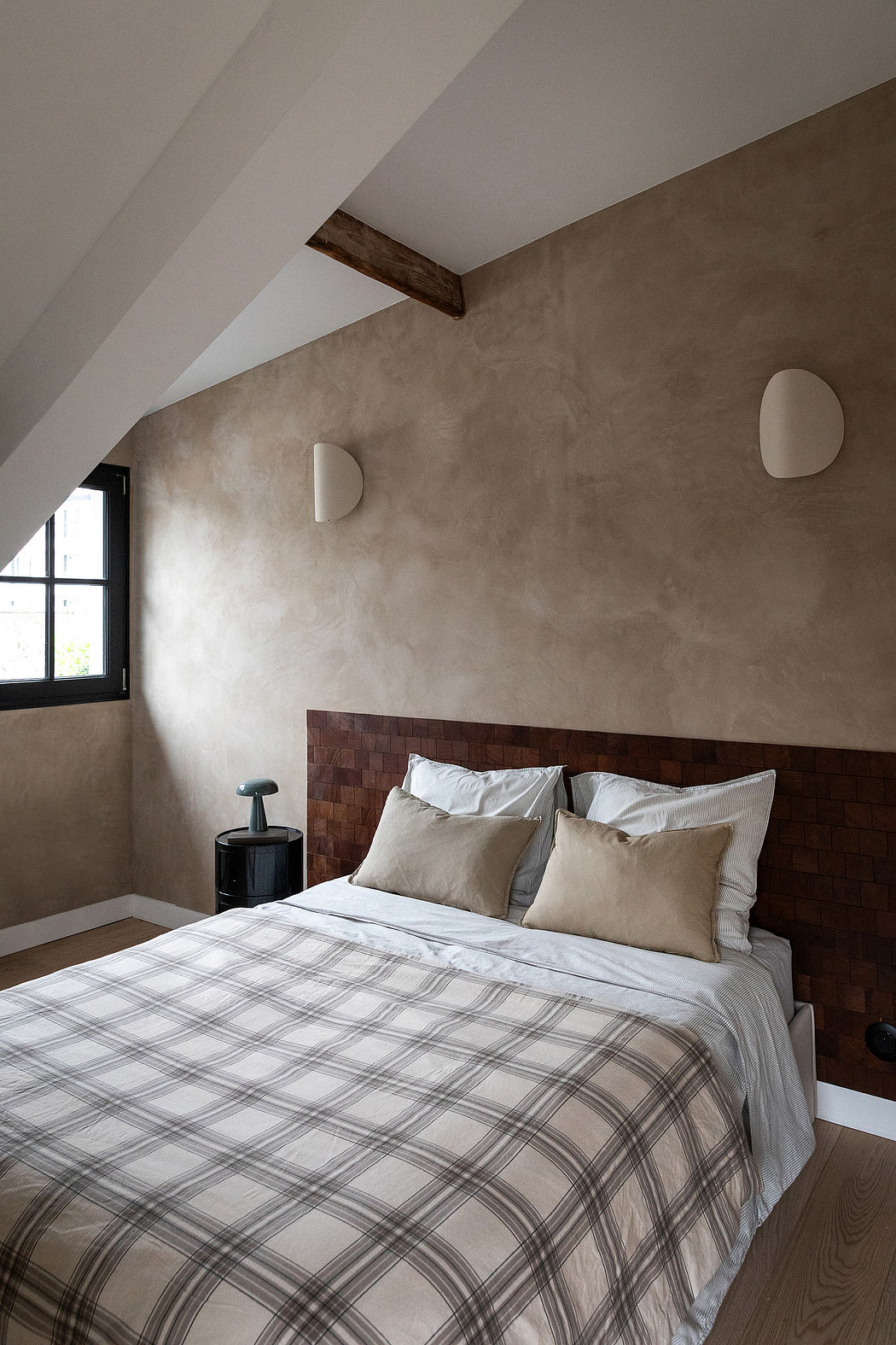 A cozy bedroom with exposed wooden beams, a plaid bedspread, and textured walls.