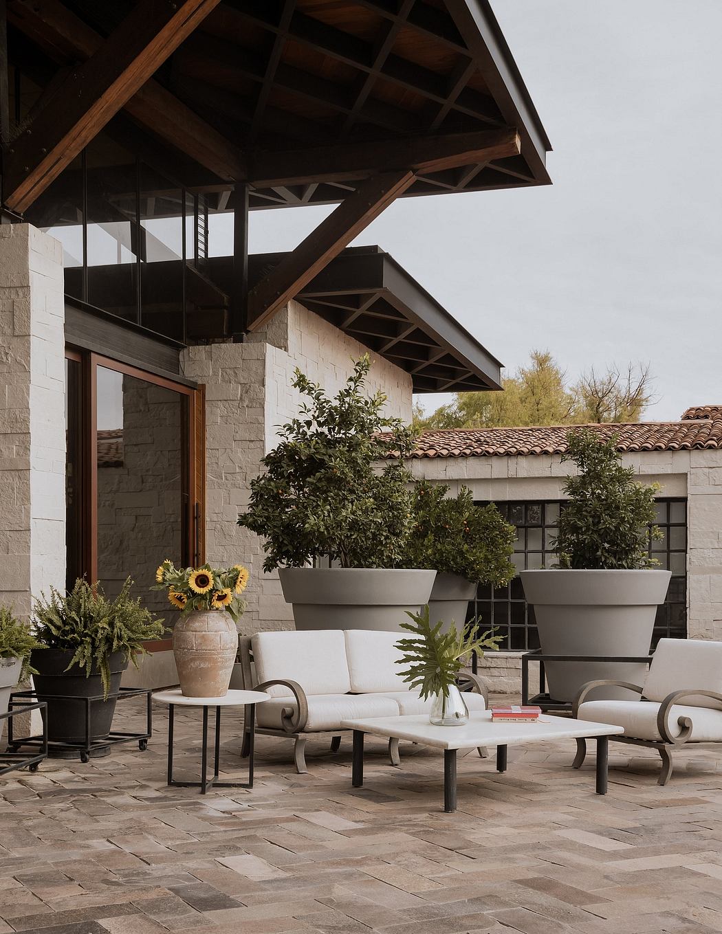 An outdoor patio with stone walls, wooden beams, and contemporary patio furniture, accented by potted plants.