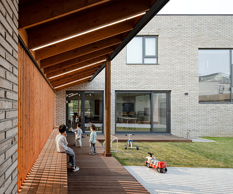 Wooden slanted roof, brick exterior, and patio with children's toys on a grassy lawn.