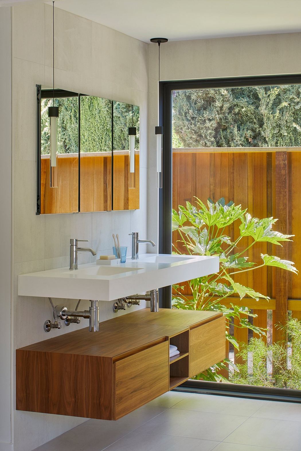 Modern bathroom with a white sink, wooden vanity, and a glass window overlooking the lush greenery outside.