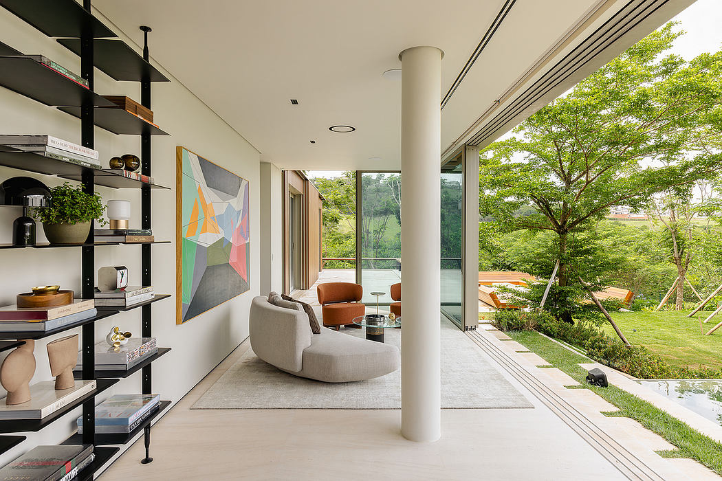 Modern open-concept living space with geometric artwork, shelving, and expansive windows overlooking lush greenery.