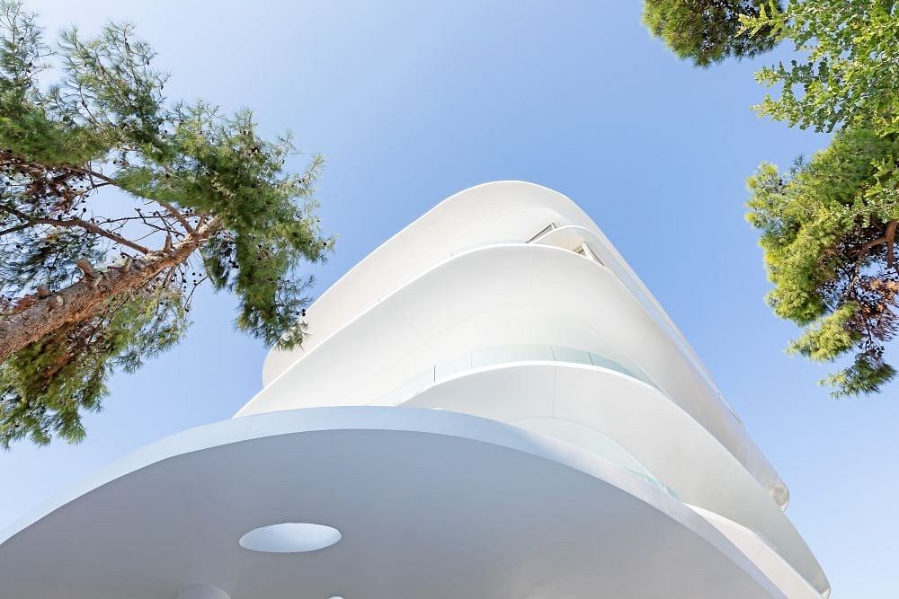 Striking modernist building with curved, white facade and surrounding trees.