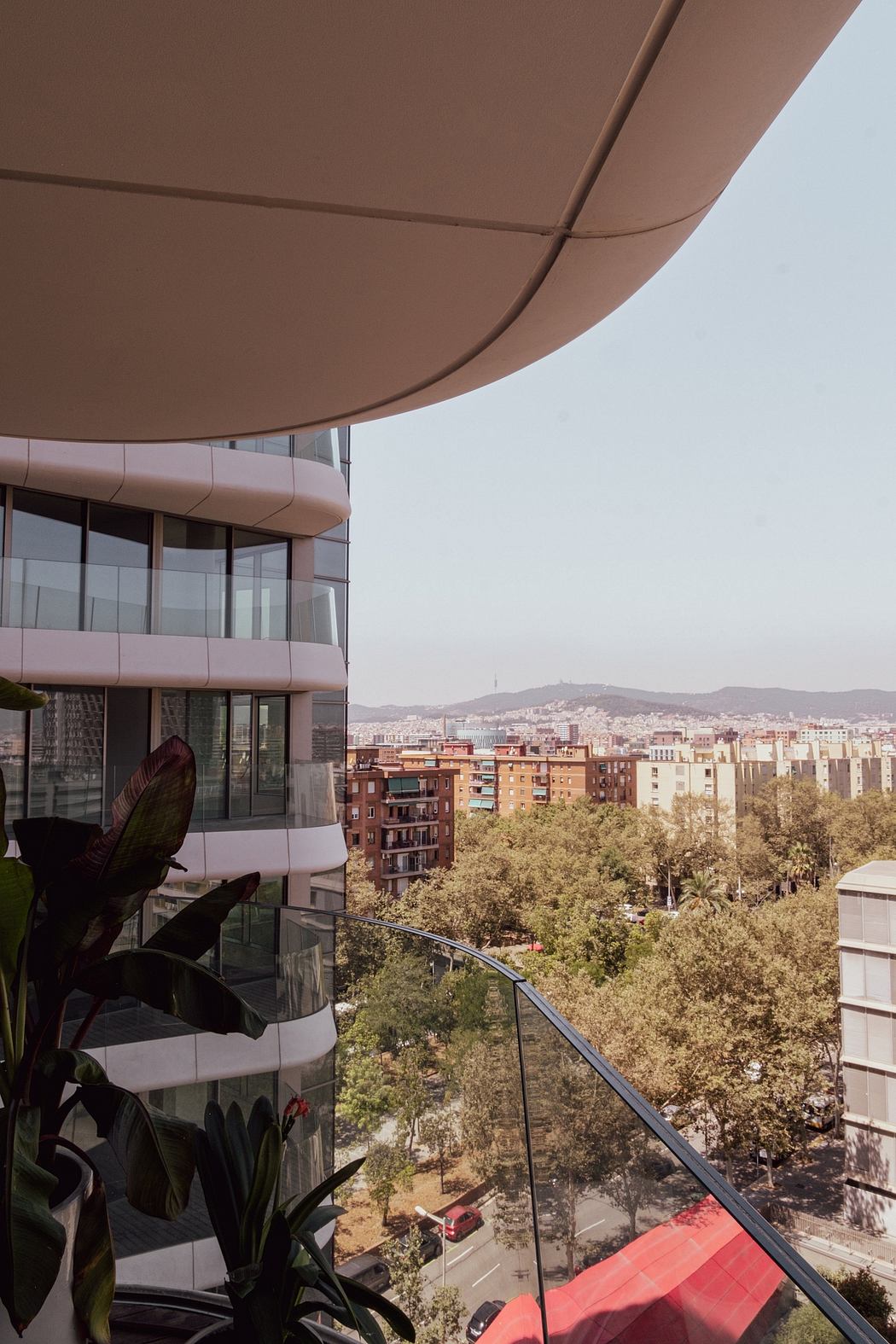 Curved modern architecture, glass balcony overlooking lush urban cityscape.