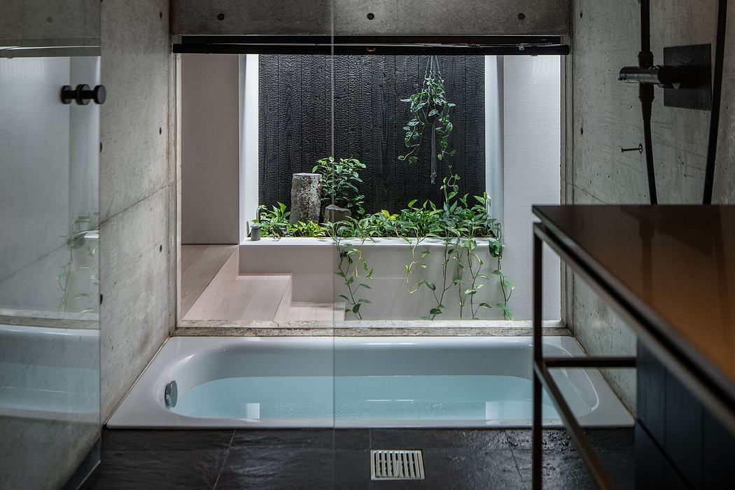 Minimalist bathroom with concrete walls, plant-filled window, and sunken bathtub.