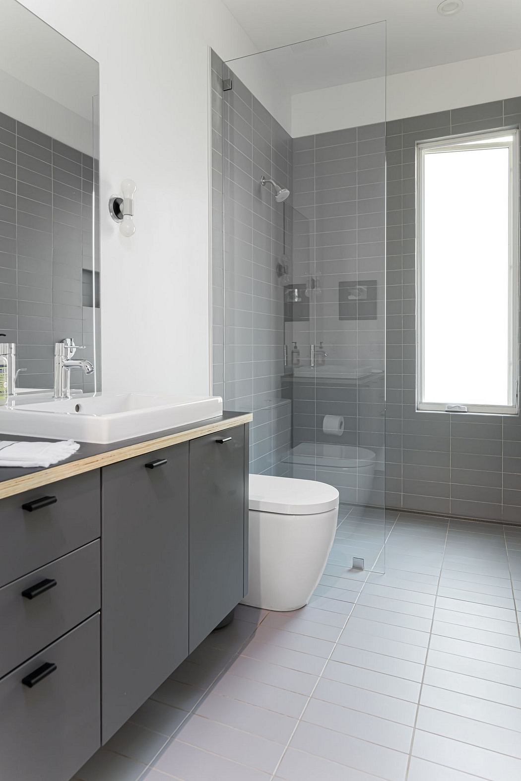 Modern, minimalist bathroom with gray tile, white basin, and wooden vanity.