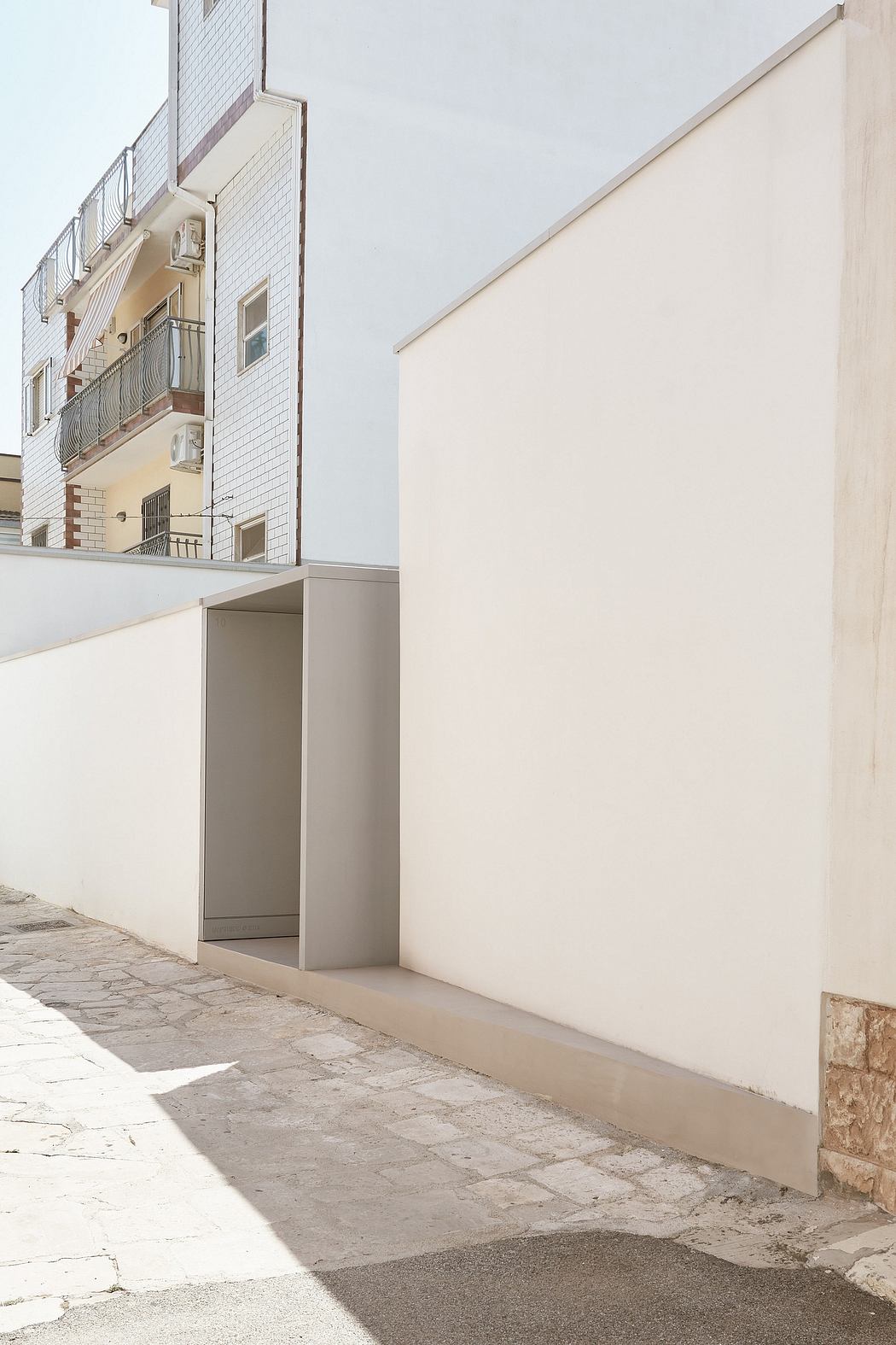 Minimalist building facade with recessed entrance and tiled walkway.