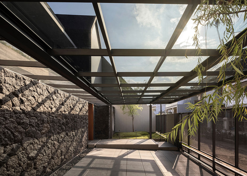 Geometric architectural structure with stone walls, glass ceiling, and greenery.