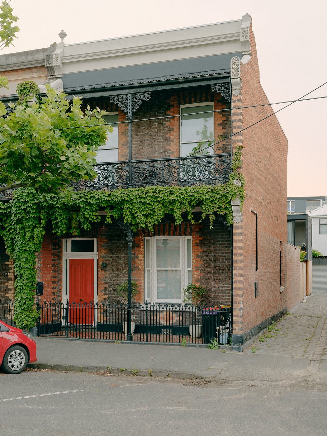Charming brick building with ornate decorative ironwork balcony and red front door.