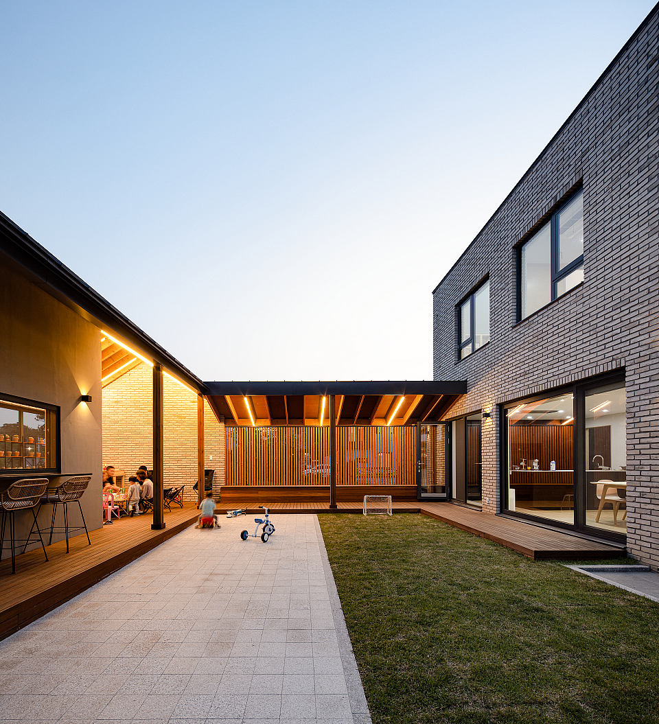 A modern courtyard with brick facades, wooden decks, and a grassy lawn; children playing.