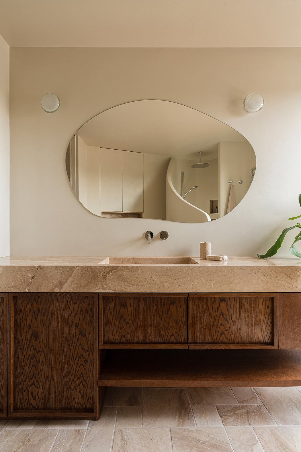 Minimalist bathroom with curved mirror, wooden vanity, and natural stone countertop.