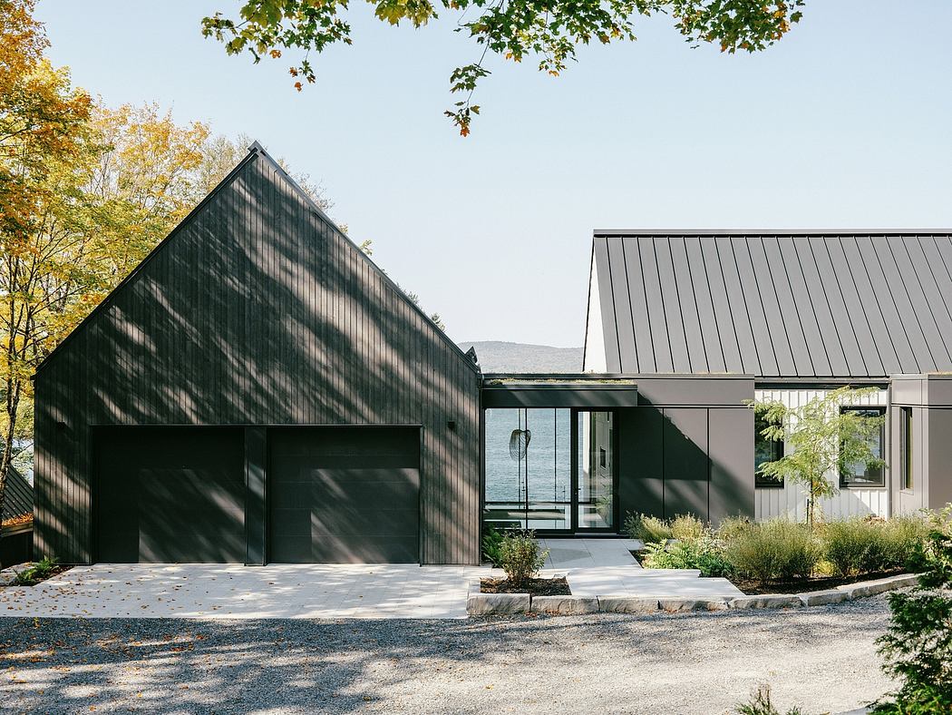 Modern architectural design with a prominent peaked roof, glass walls, and dark siding. Minimal landscaping enhances the clean lines.