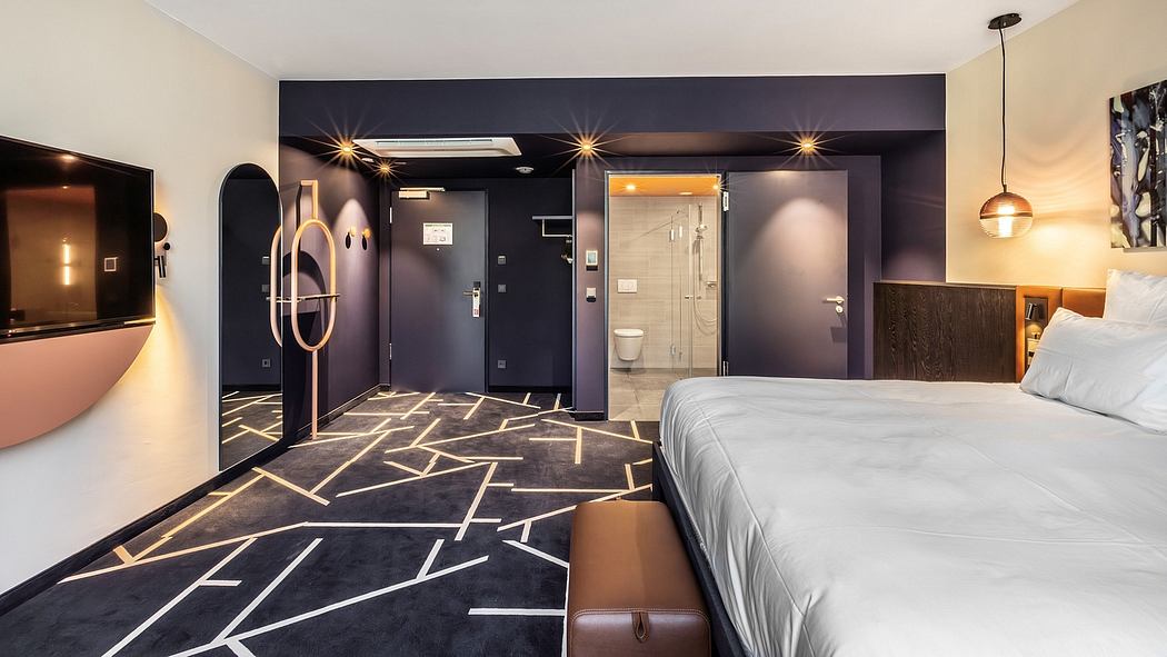 A modern hotel room with a geometric patterned floor, dark walls, and an en-suite bathroom.