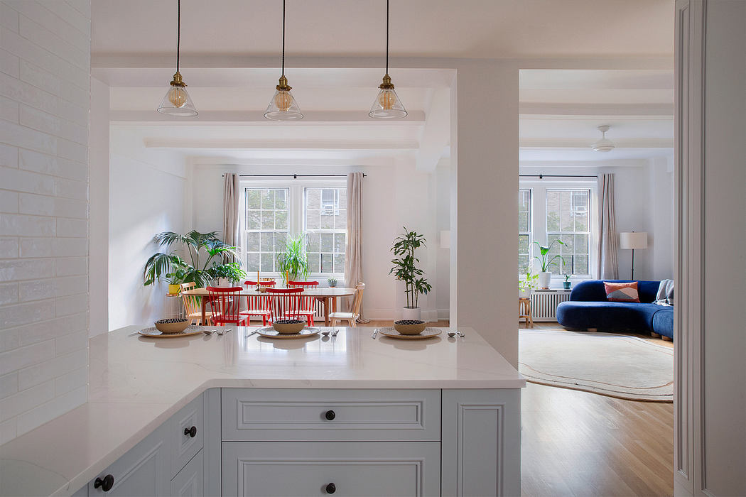 Open-concept kitchen with white cabinets, pendant lights, and a view of a living room with a blue sofa.