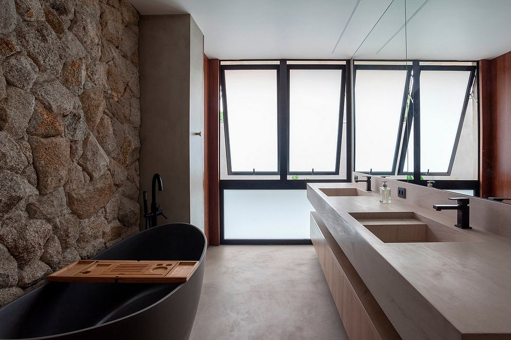 Rustic stone wall, modern vanity, large windows flood the spacious bathroom with light.