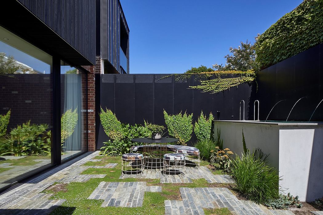 A modern courtyard with a sleek black exterior, lush greenery, and a minimalist seating area.