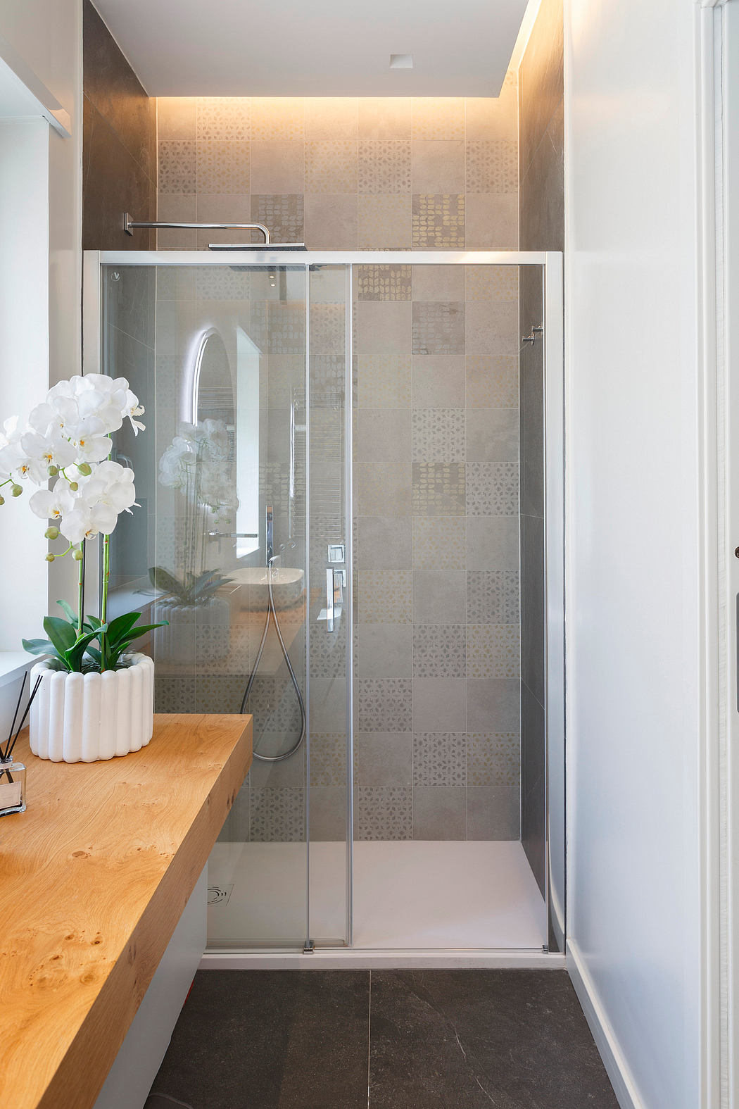 Modern minimalist bathroom with glass walk-in shower, wood vanity, and potted orchid.
