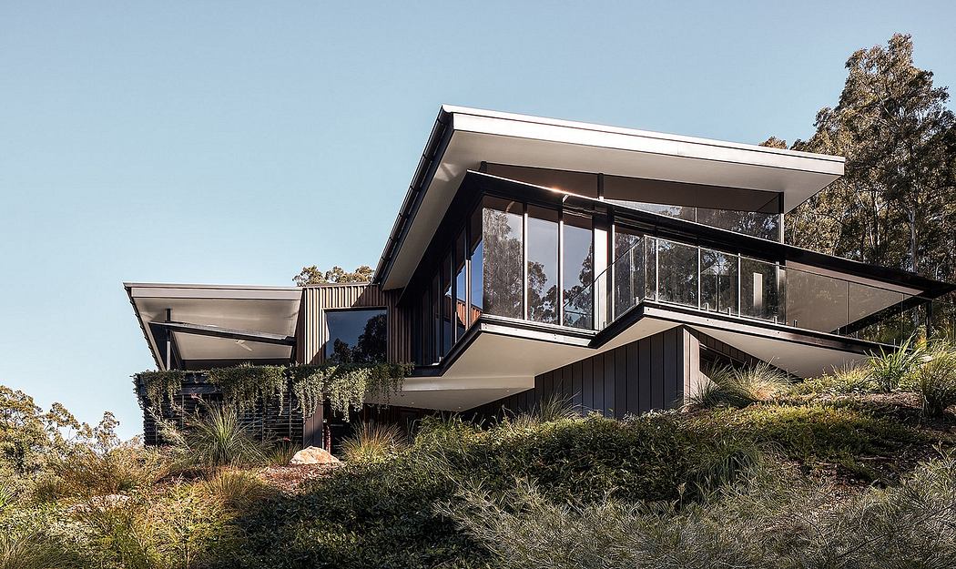 Modern, cantilevered house with large glass windows, wooden siding, and lush landscaping.