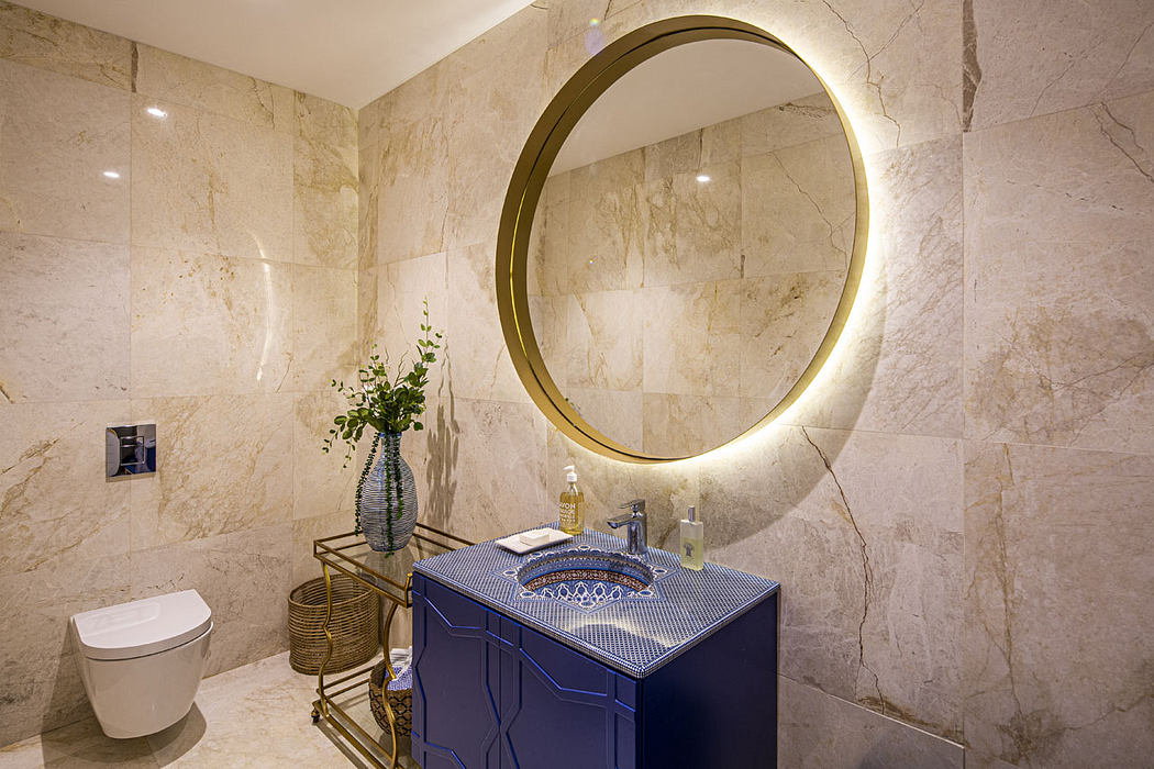 Elegant bathroom with circular gold-framed mirror, patterned blue vanity, and marble walls.
