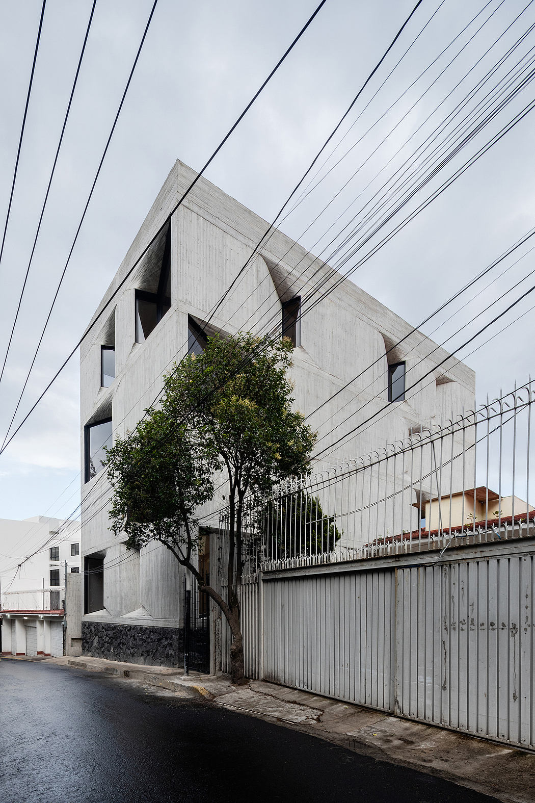 A concrete, angular building with asymmetrical windows and a tree protruding through the facade.