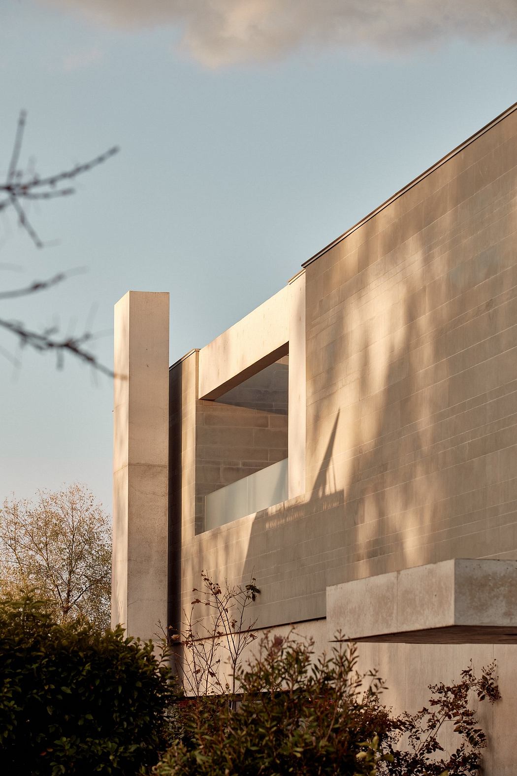 A modern concrete building with geometric patterns, contrasting shadows, and lush vegetation.