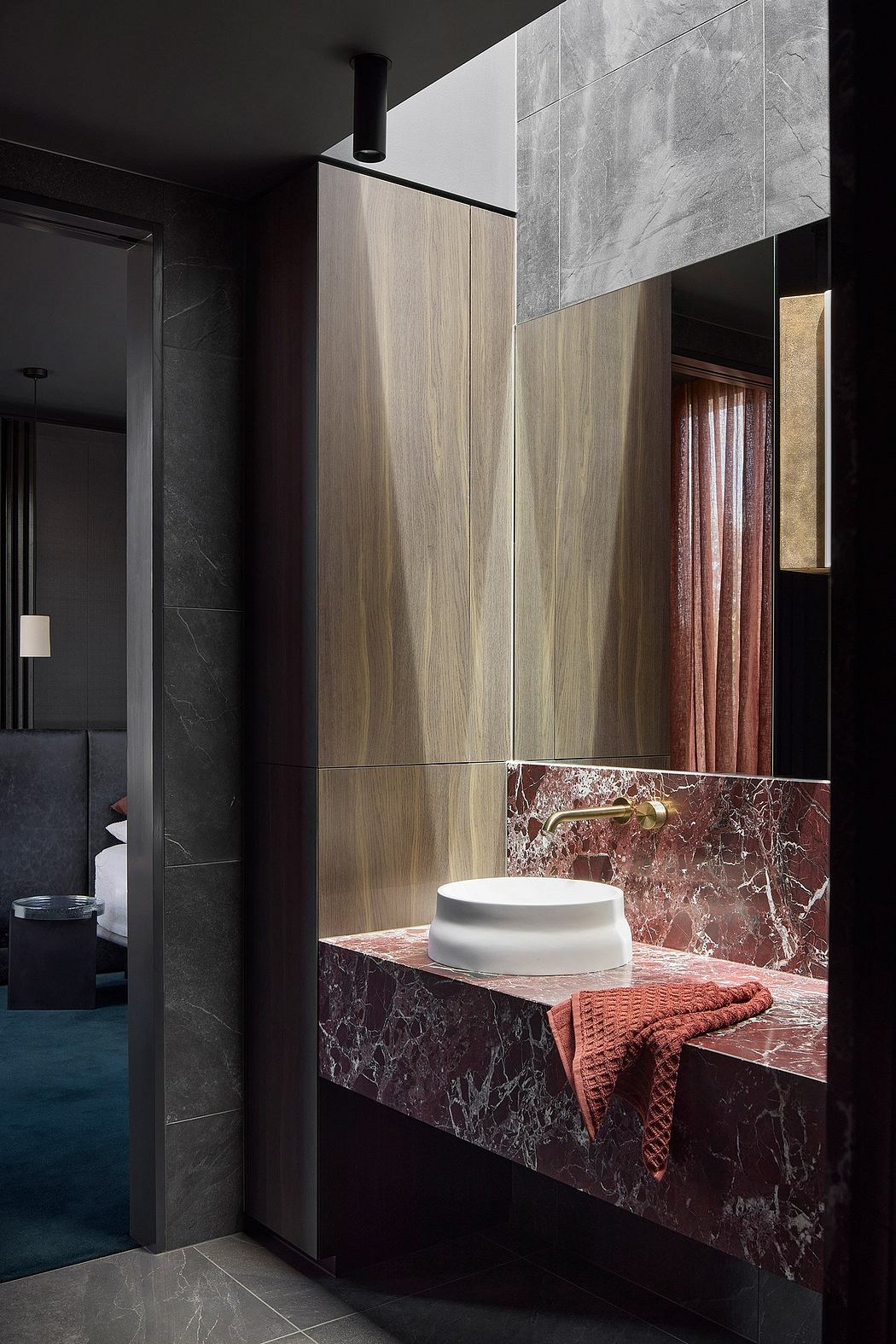 Dark, modern bathroom with contrasting wood and marble vanity, vessel sink, and plush towel.