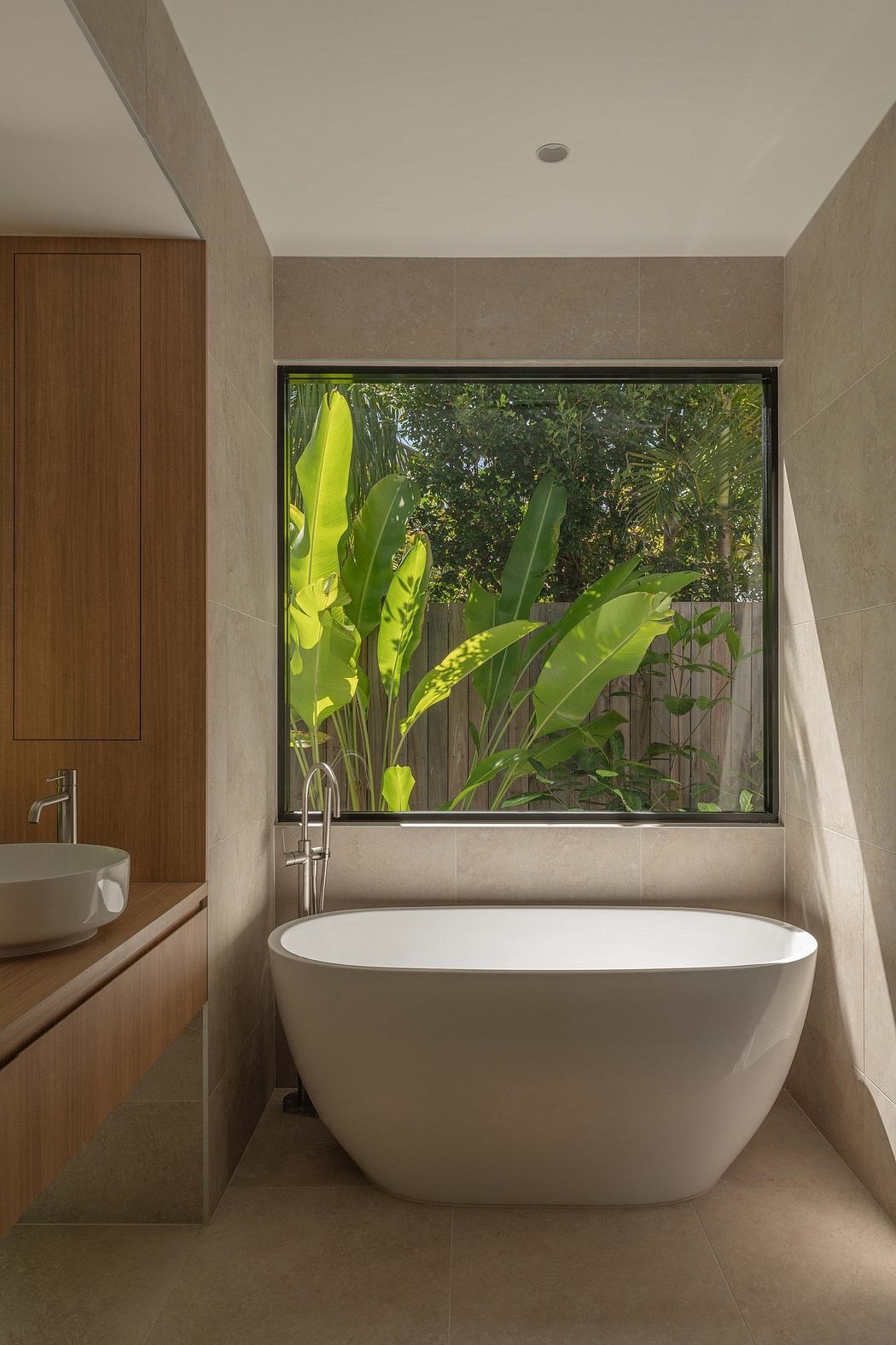 A modern bathroom with a freestanding tub overlooking a lush, tropical garden.