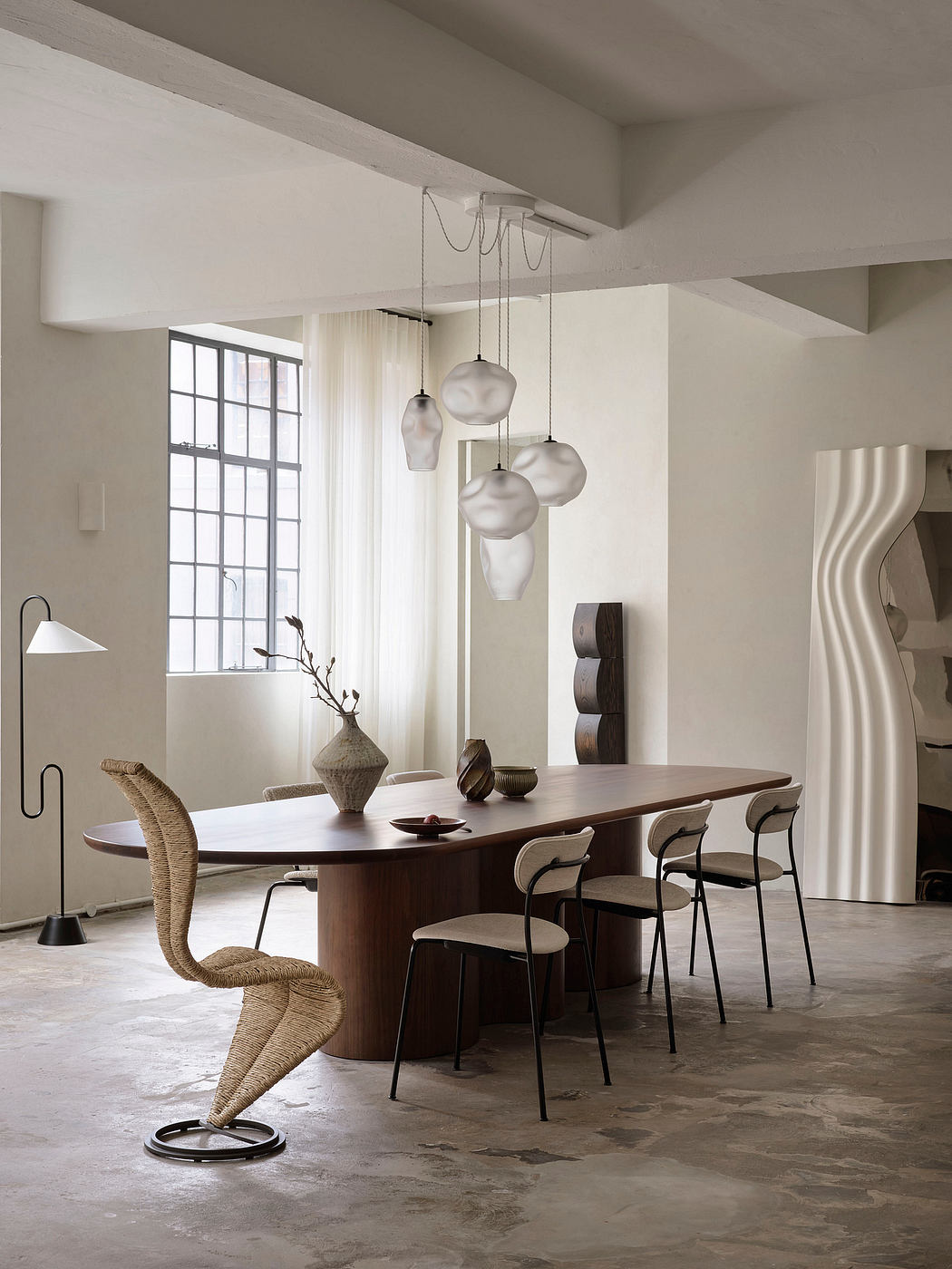Minimalist dining room with a wooden table, chairs, and pendant lighting fixtures.