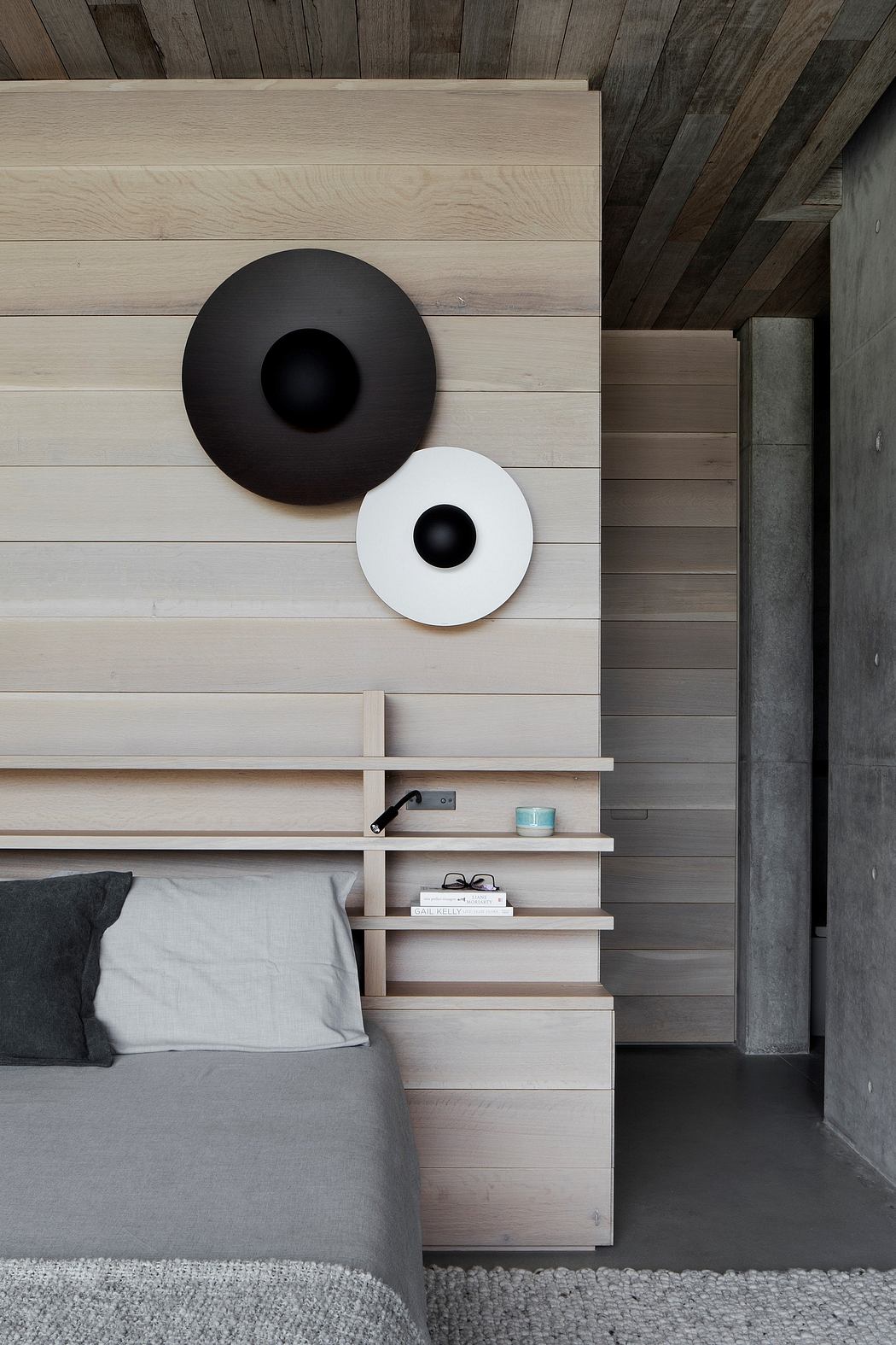 The bedroom features minimalist decor with contrasting black and white circular shapes on the wall, wooden shelves, and a gray bedspread.