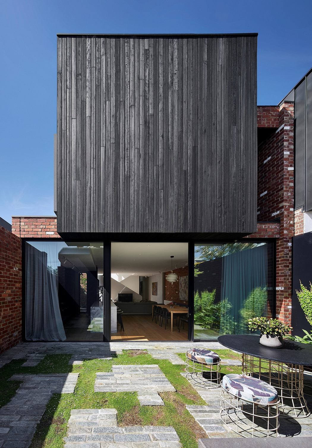 Modern exterior with black vertical wood panels, large glass walls, and a lush green courtyard.