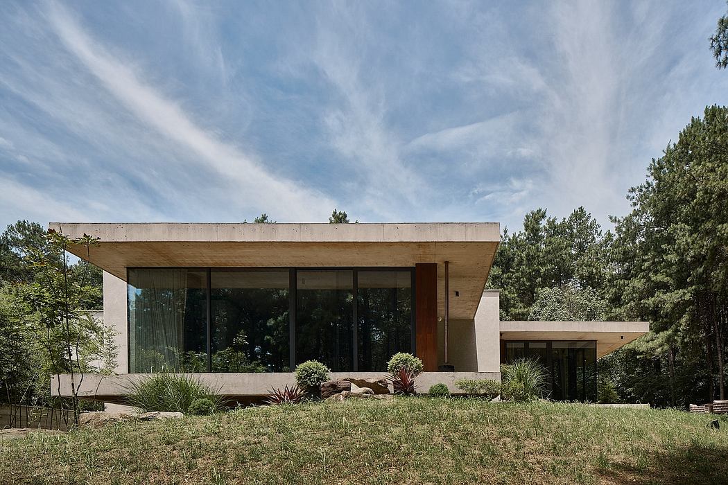 A modern, single-story home with large glass windows, a flat roof, and a natural landscape.