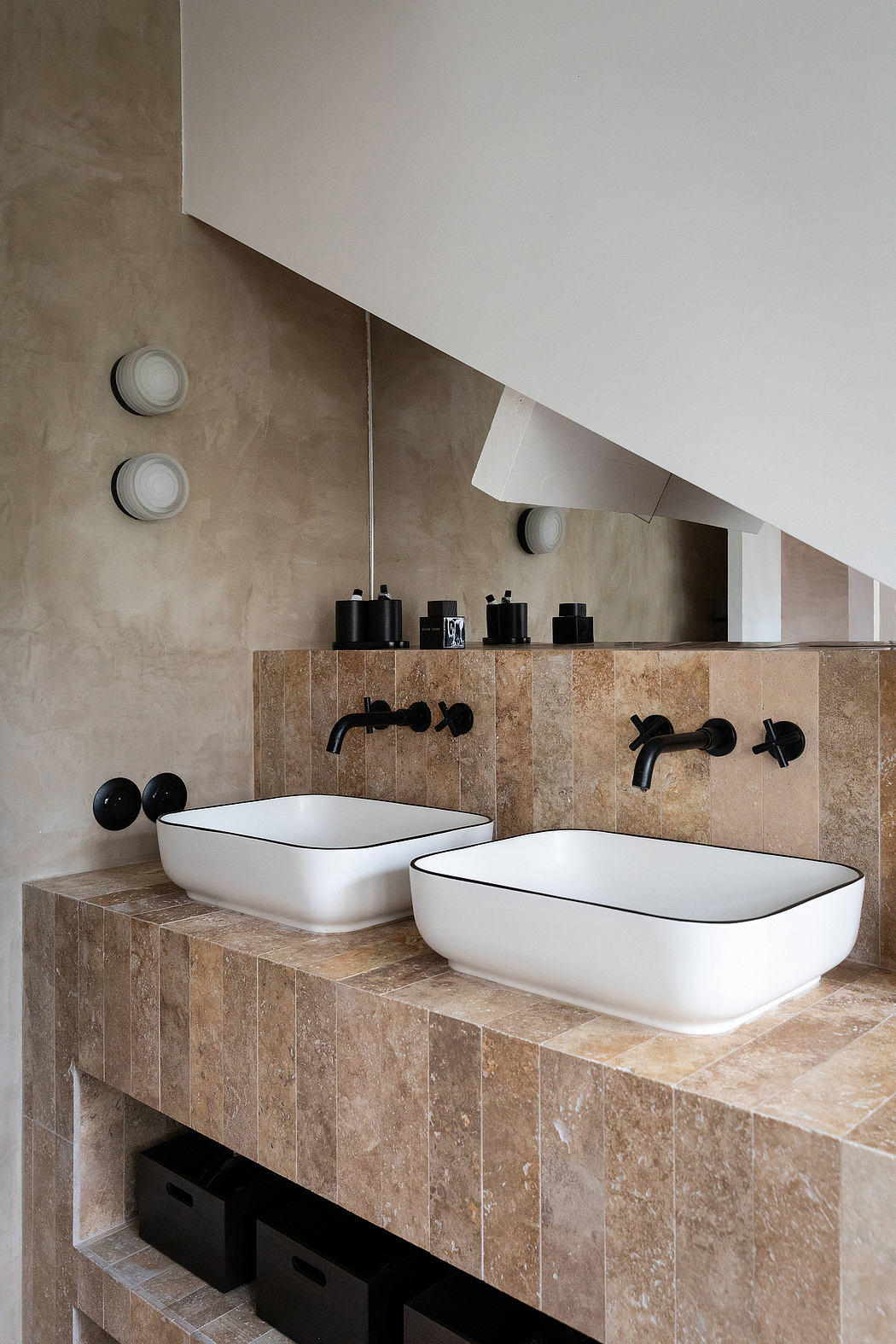 Modern bathroom with stone-tiled vanity and minimalist white vessel sinks, black faucets.
