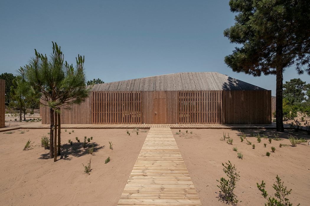 A modern wooden structure with a slanted roof, surrounded by sparse vegetation and a wooden walkway.