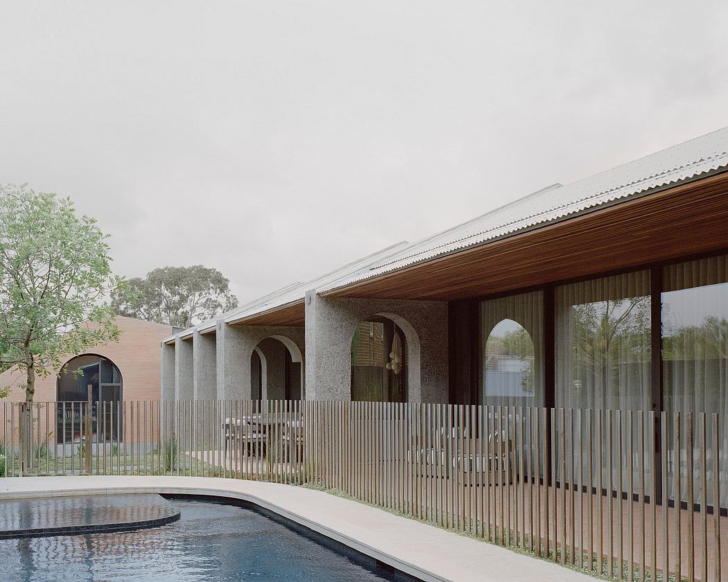 Arched wooden and glass entrance with a porch and reflecting pool surrounded by trees.