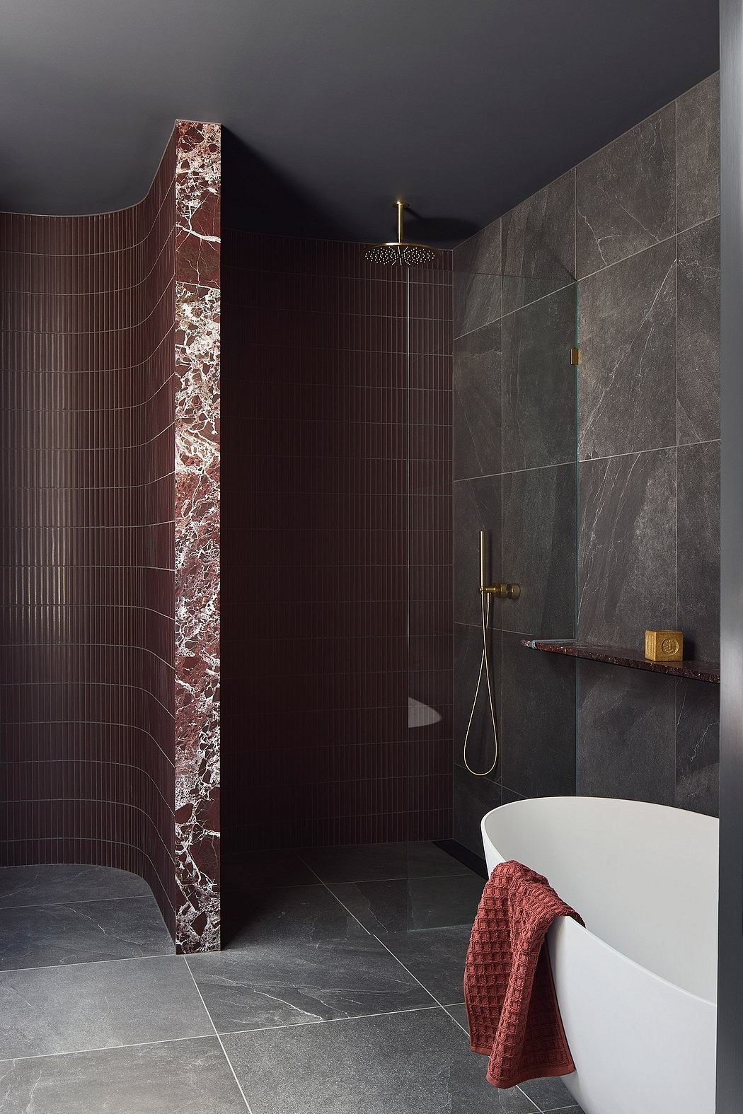 A dark, luxurious bathroom with marble walls, a freestanding tub, and a modern shower fixture.