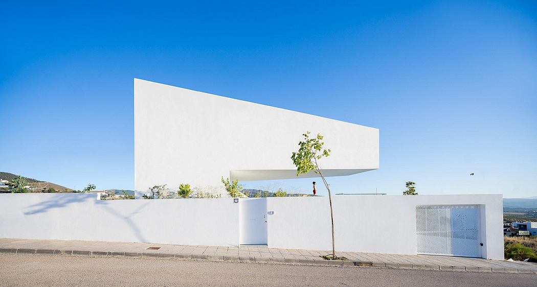 Striking white angular building with minimalist design and a single tree against a blue sky.