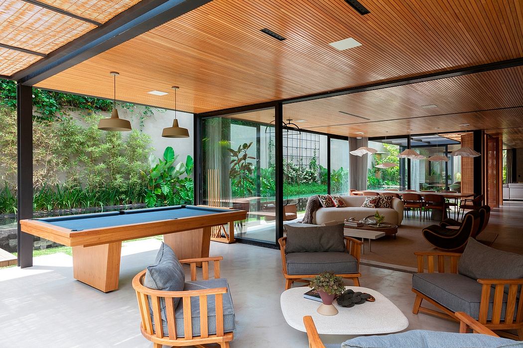 Spacious indoor-outdoor living space with wooden ceiling, furniture and greenery.